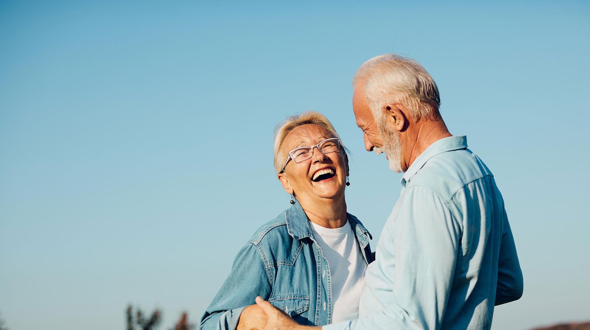 An elderly couple sharing a joyful moment outdoors with blue skies.