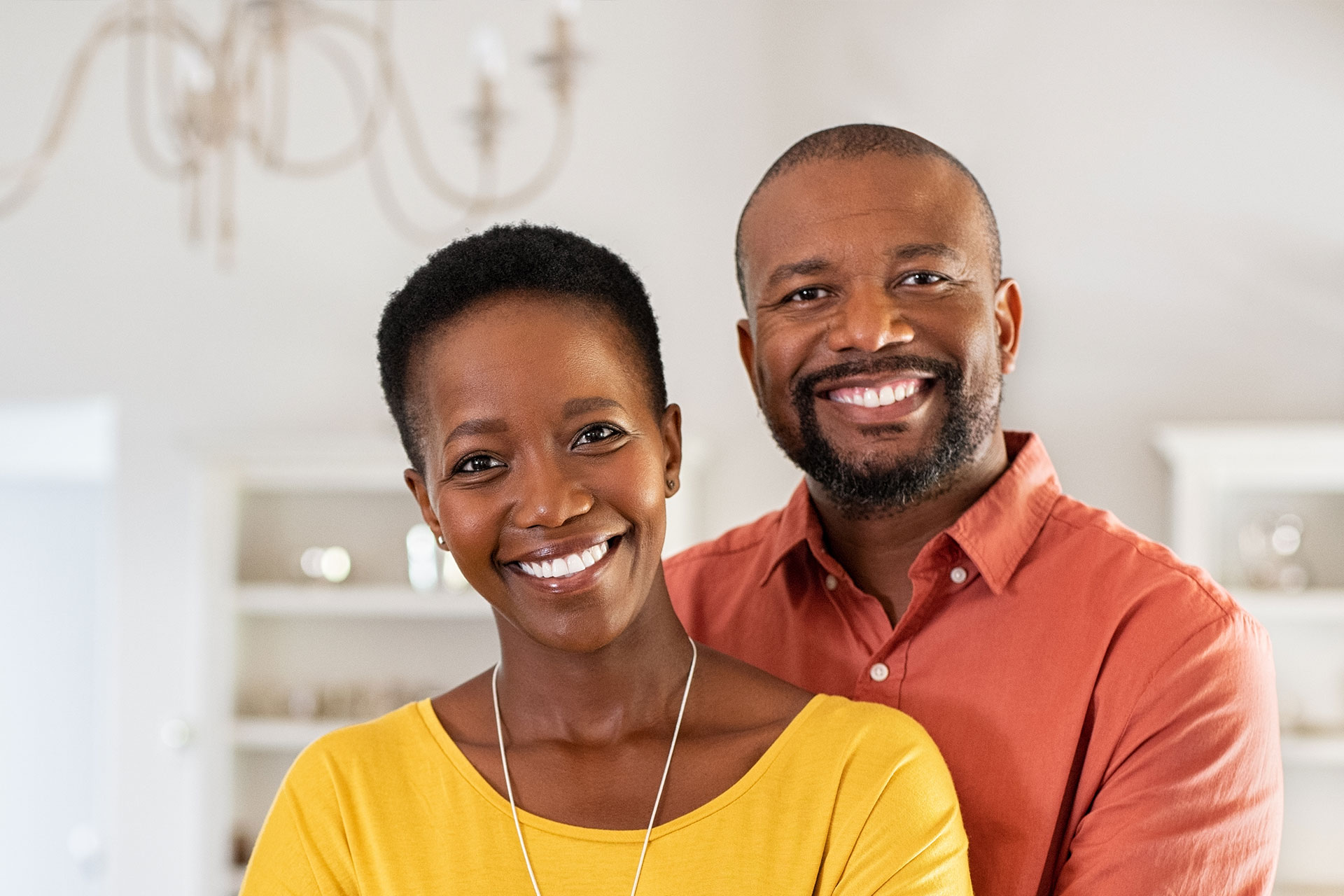 A man and a woman, both smiling, posing together in front of a kitchen cabinet.