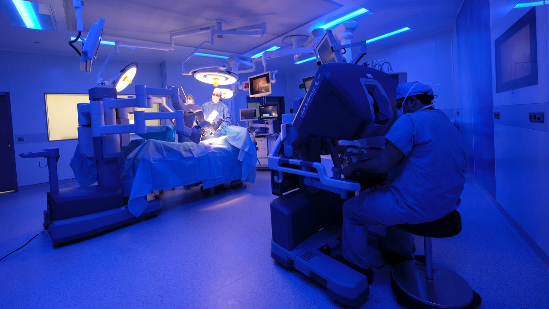 The image shows an operating room with medical equipment, personnel in surgical attire, and a blue color scheme.