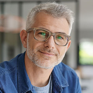 A man with a beard and glasses, wearing a denim jacket, smiles at the camera.